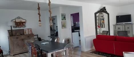 A dining area with a table and chairs, a red sofa, a TV, and a kitchen in the background.