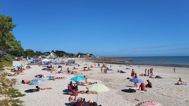 Ein Strand mit Menschen, die sonnenbaden und schwimmen, Sonnenschirmen und Gebäuden direkt am Strand.
