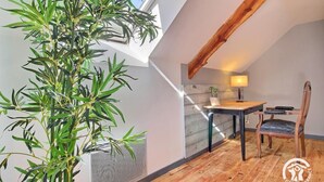 Un acogedor cuarto ático con techo de madera, una mesa de comedor con sillas, una planta pequeña y una ventana con vista al cielo.