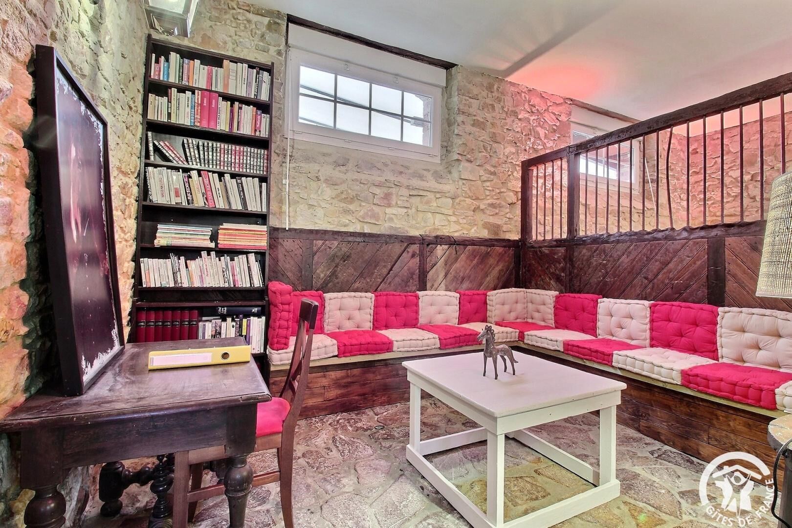 A cozy room with a stone wall, a bookshelf, a cushioned sofa, and a small table.