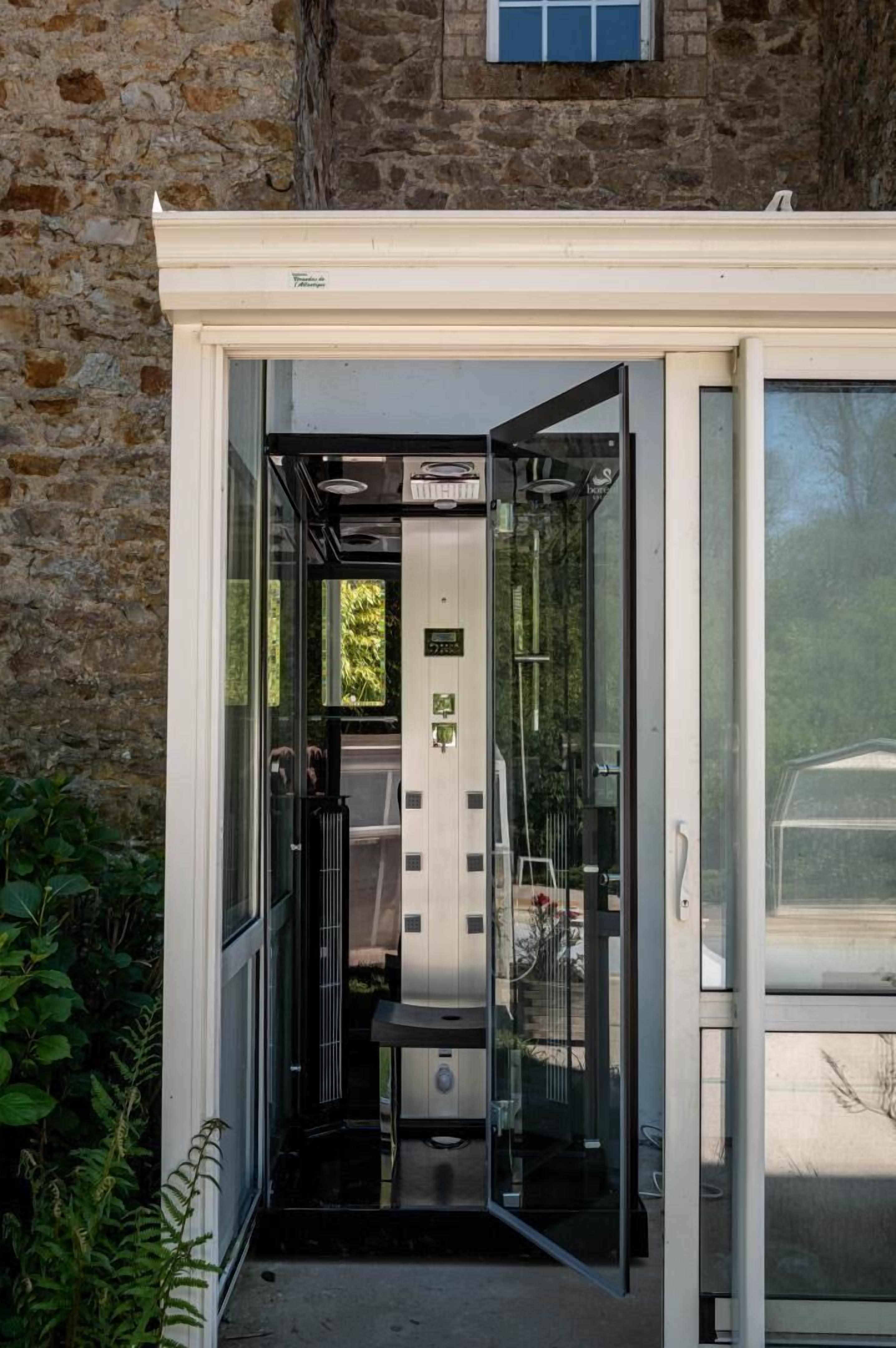 An open glass door leading to a room with a bed, a small table, and a chair.