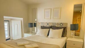 Habitación de hotel con una cama grande, dos mesitas de noche, un tocador, un espejo y una ventana.