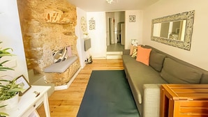 Una sala de estar con pared de piedra, un sofá gris, piso de madera y un espejo en la pared.