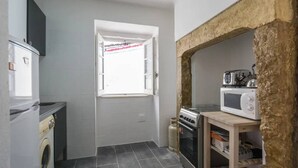 A compact kitchen with a washing machine, a microwave, and a stove. - Charming Alfama Flat (Lisboa)