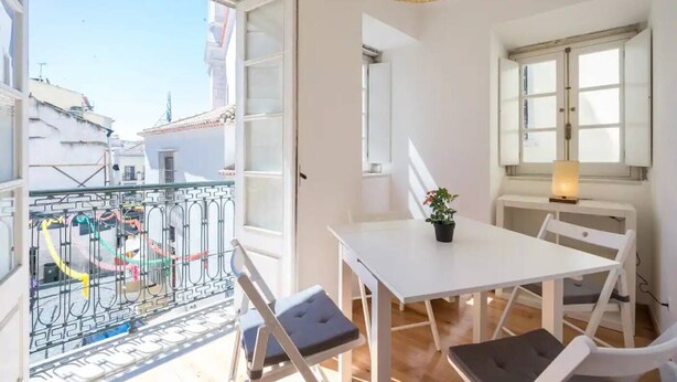 A bright room with a white table, chairs, and a balcony with a metal railing. - Charming Alfama Flat (Lisboa)