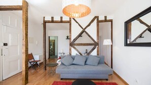A modern living room with a grey sofa, wooden beams, a red rug, and a hanging light fixture. - Charming Alfama Flat (Lisboa)
