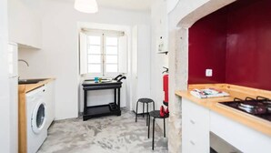A compact kitchen with a washing machine, a small table, and a red wall.