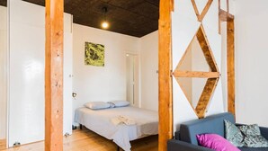 A room with a bed, a sofa, wooden beams, a hanging light, and a door.