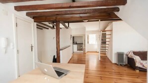 Ein geräumiges Loft mit freiliegenden Holzbalken, einer Küche im Hintergrund und einem Laptop auf einem Tisch.