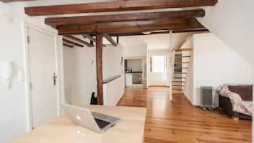 Un loft spacieux avec des poutres apparentes, une cuisine à l’arrière-plan et un ordinateur portable posé sur une table.