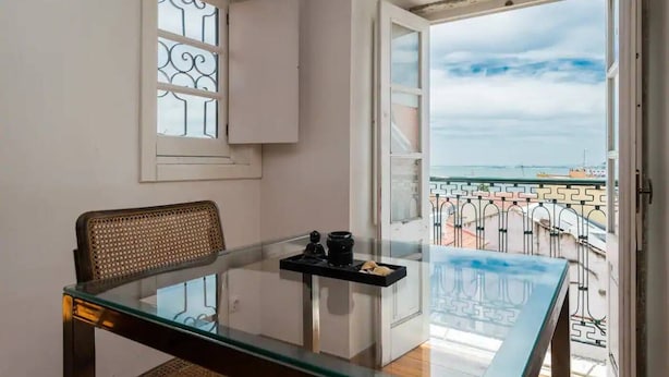 Ein Balkon mit Glastisch und Stuhl, ein Fenster mit Verzierungen und Blick auf das Meer und Boote.