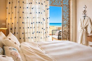 A hotel room with a bed, a view of the beach, and a robe hanging on the wall.