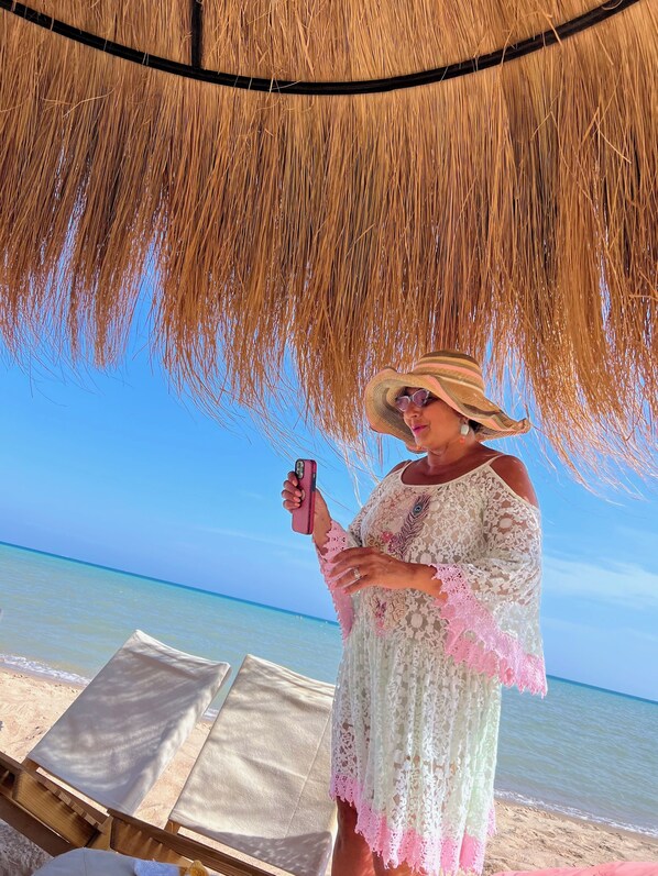 A beach scene with a straw umbrella, a person in a white lace dress, and a clear blue sky.