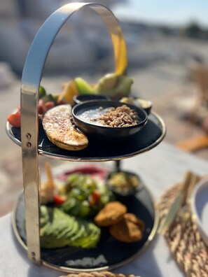 A three-tiered serving tray with various food items, including a bowl of cereal, a plate of sliced vegetables, and a plate of nuts.