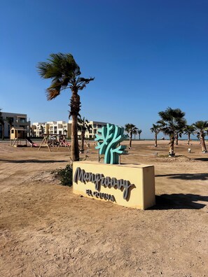 A sign for Mangrove El Gouna with a desert landscape and palm trees in the background.