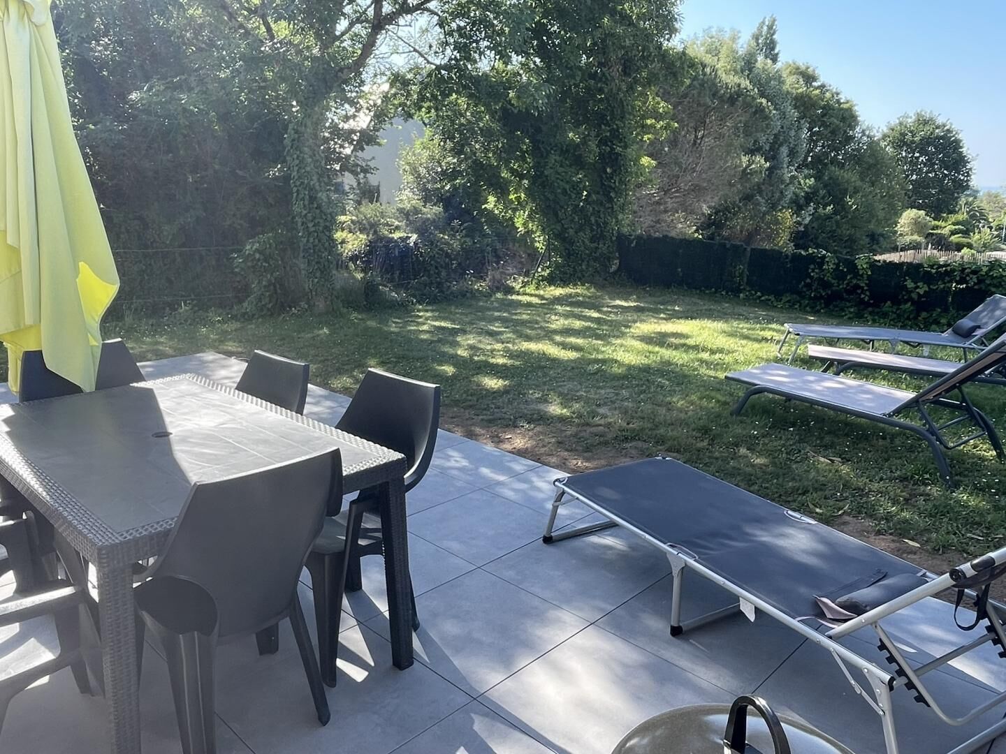 Une terrasse avec une table et des chaises, une chaise longue et un espace abrité.