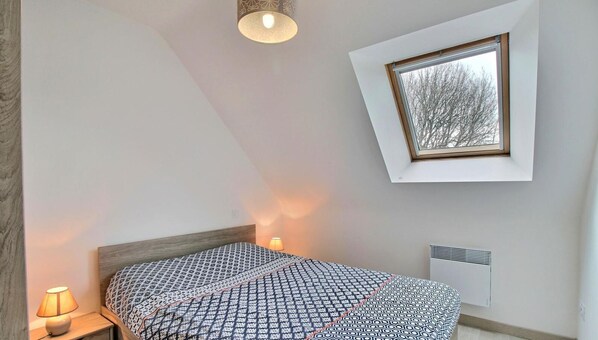 Un dormitorio con una cama, una lámpara de noche, un cuadro en la pared y una ventana.
