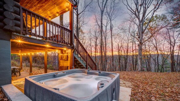 Un jacuzzi frente a una cabaña de madera con una terraza y escaleras que conducen a un nivel superior.
