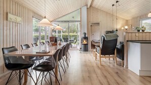Une vaste salle à manger avec une longue table et des chaises, une cheminée centrale et une vue sur l’extérieur grâce à de grandes fenêtres.