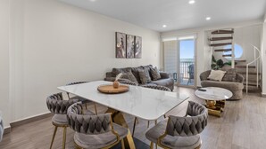 A modern living room with a dining table, grey upholstered chairs, a sofa, and a staircase leading to a balcony. - BahiaMar Luxury Oceanfront Oasis (South Padre Island)