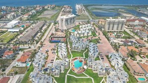 An aerial view of a resort with multiple buildings, a central swimming pool, and surrounding greenery. - BahiaMar Luxury Oceanfront Oasis (South Padre Island)