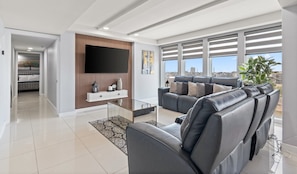 A modern living room with a sofa set, a flat-screen TV, and a view of the city. - Solare Tower Sunset Panorama Paradise (South Padre Island)