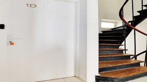 A white door with a "1D" label, a black spiral staircase, and a small window in the background.
