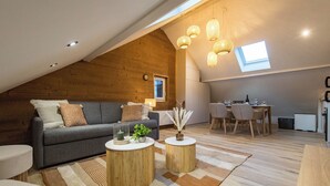 Un appartement moderne de style « loft », avec un plafond en pente, un canapé gris, un coin repas et une cuisine.