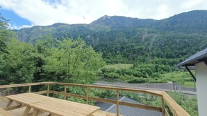 Une terrasse en bois avec des tables de pique-nique, offrant une vue sur un paysage montagneux.