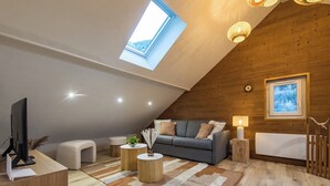 Une chambre de style loft moderne, avec un plafond en pente, un puits de lumière, un canapé gris, un plancher en bois et une table de chevet avec une lampe.
