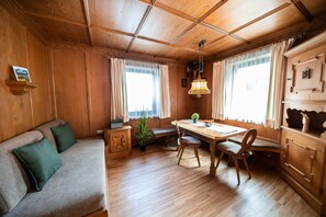 Interior acogedor de una cabaña con techo de madera, una mesa de comedor con sillas, un sofá con cojines y una radio sobre un mueble.