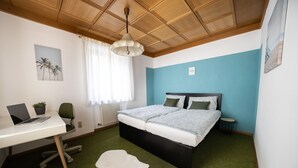 Une chambre à coucher avec un lit, un bureau avec un ordinateur portable, une chaise, un radiateur et une fenêtre avec des rideaux.