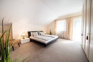 Un dormitorio con cama, mesitas de noche, lámpara, sillón y una planta.