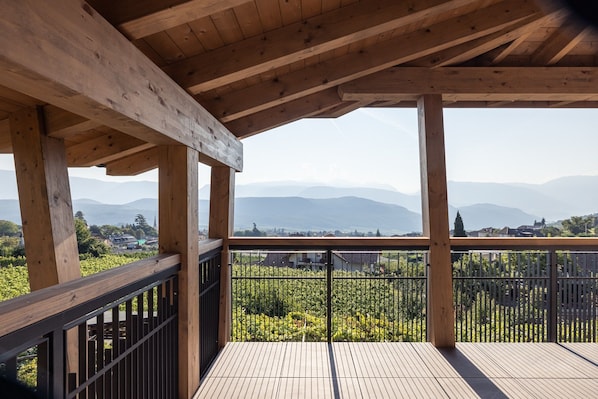 Un balcón de madera con vistas a un viñedo y montañas al lejano.