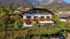 Un edificio a due piani con tetto spiovente, diverse finestre e un balcone con piante.