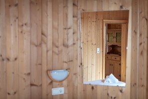 A wooden interior with a small window, a towel on the floor, and a wall-mounted light fixture.