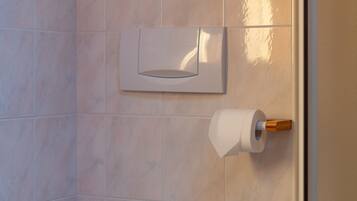 Ein Badezimmer mit Toilette, Papierhandtuchspender und Toilettenpapierhalter an der Wand.