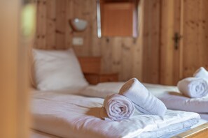 A wooden room with a bed, pillows, and a rolled towel.