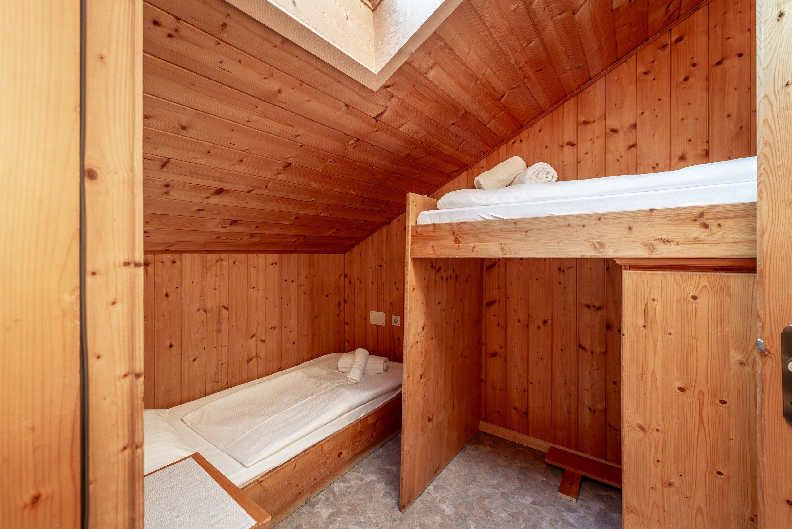 Eine kleine Holzhütte mit einem Etagenbett und einem Einzelbett, beide mit weißer Bettwäsche.