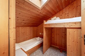 Una pequeña cabaña de madera con una litera y una cama individual, ambas con ropa de cama blanca.