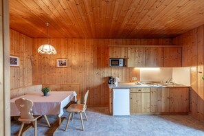 Cocina compacta con paredes de madera, zona de comedor con mesa y sillas, microondas y lavamanos.