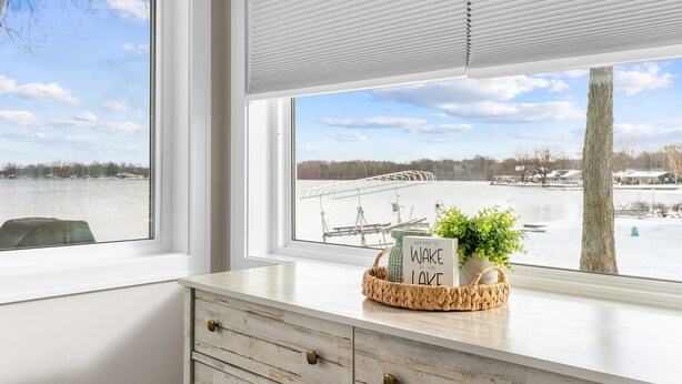 Una habitación con vista a un lago, un aparador de madera con cajones, una cesta con un letrero y una planta en maceta.