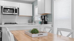 Una cocina moderna con armarios blancos, microondas, cafetera y una mesa de comedor con sillas.