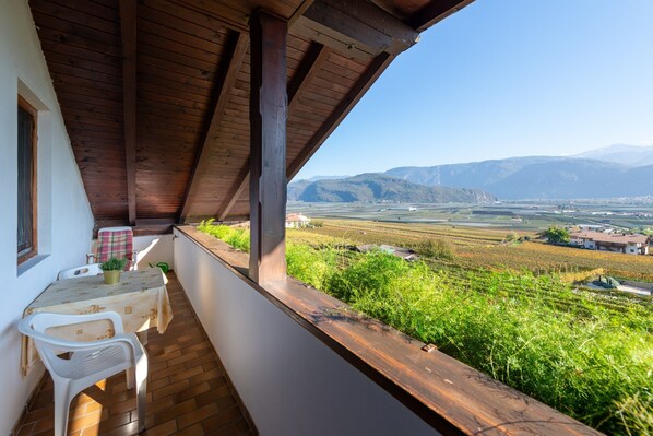 A balcony with a table and chairs, overlooking a vineyard and distant mountains.