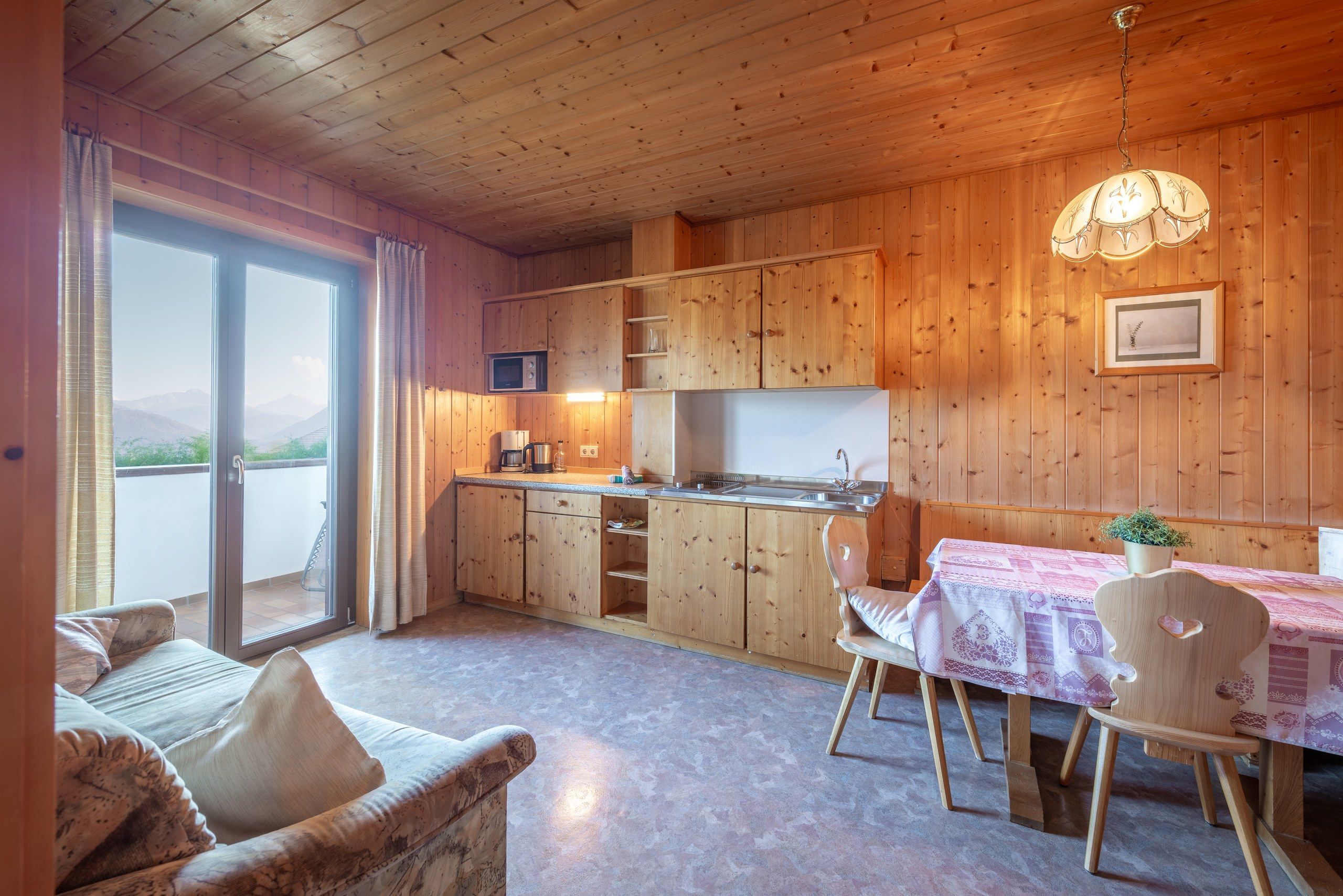 Une cuisine chaleureuse avec des meubles en bois, une table à manger avec des chaises et une vue sur l’extérieur grâce à une porte coulissante.