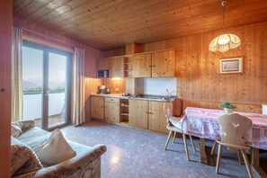 A cozy kitchen with wooden cabinets, a dining table with chairs, and a view of the outdoors through a sliding door.