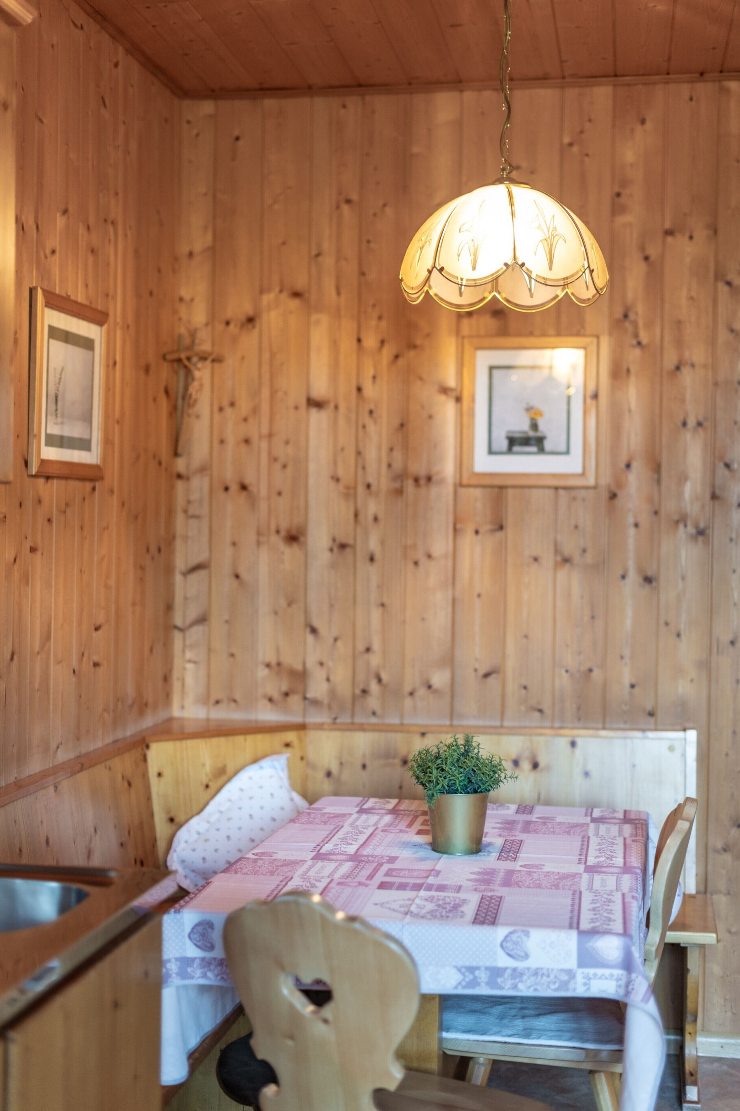 Un interno in legno con un tavolo, sedie, una lampada a sospensione e quadri appesi al muro.