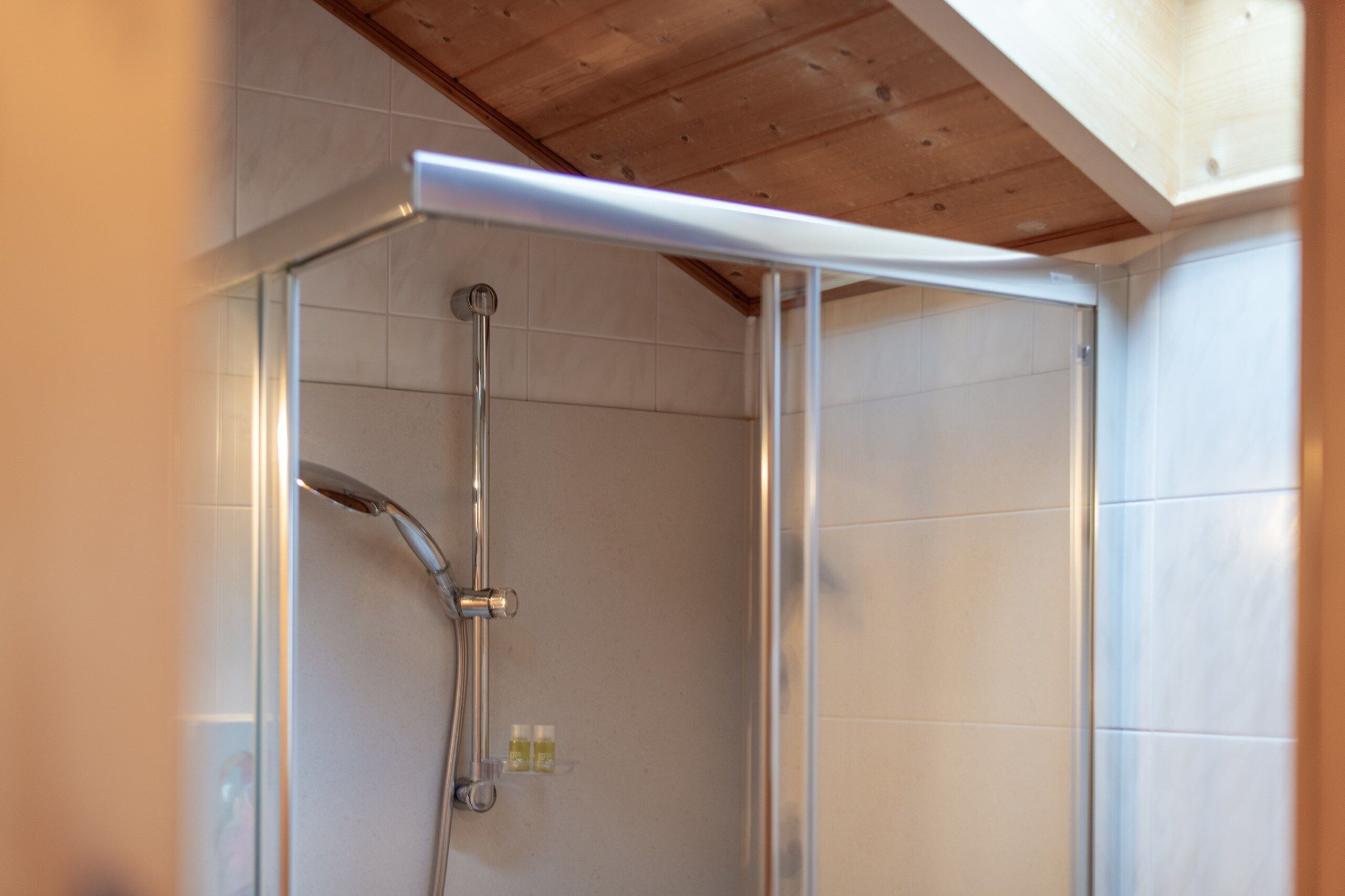 Une douche avec une porte en verre et un plafond en bois.