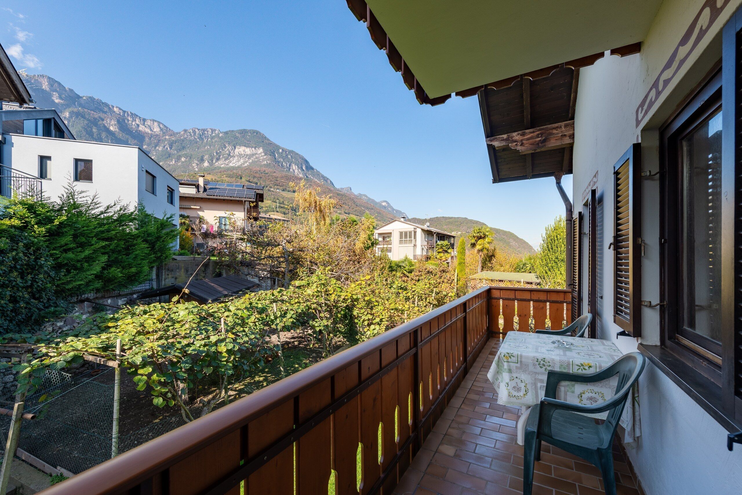 Ein Balkon mit Tisch und Stühlen, der auf einen Garten mit Bergblick führt.
