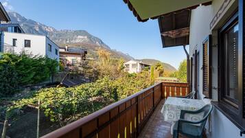 Ein Balkon mit Tisch und Stühlen, der auf einen Garten mit Bergblick führt.